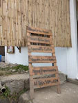 A wooden signboard is propped against a bamboo wall. The sign lists offerings such as vegetarian/vegan food, South Indian fare, speciality coffee, juices, smoothies, hemp experiments, and displays the hours of operation from 9 AM to 10 PM daily.