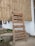 A wooden signboard is propped against a bamboo wall. The sign lists offerings such as vegetarian/vegan food, South Indian fare, speciality coffee, juices, smoothies, hemp experiments, and displays the hours of operation from 9 AM to 10 PM daily.