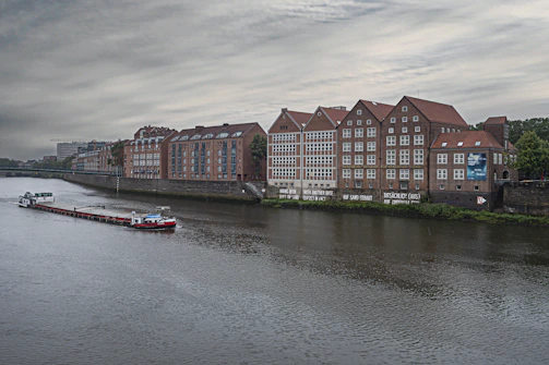 A vintage industrial river town with weathered brick buildings and smokestacks fading into morning haze.