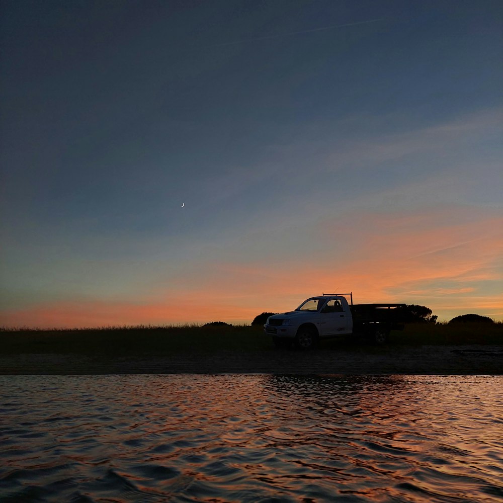 a truck is parked on the shore at sunset