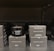 A black scented candle labeled 'Cachemire Bourbon' is placed among several black boxes labeled 'Scented Candle' and 'Oriental Woody.' The boxes and candle are displayed on a dark shelf, with the candle in the center.