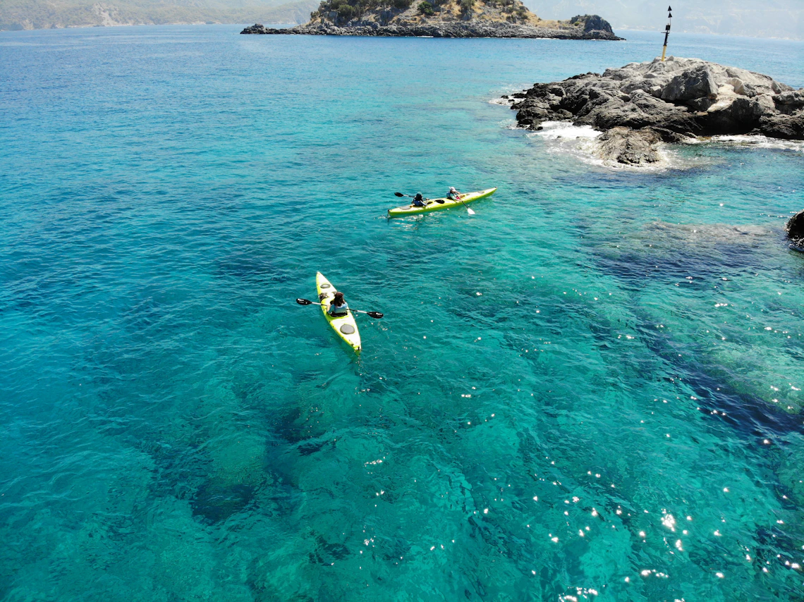 Two kayakers paddling across clear turquoise coastal water