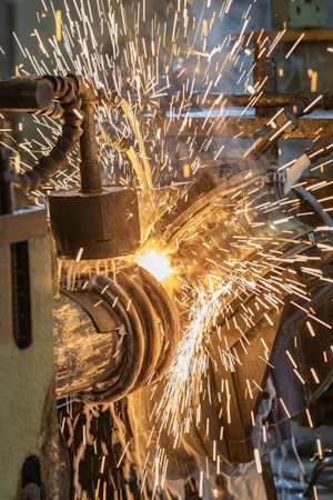 A close-up of sparks flying as a metalwork process is taking place. The image captures the vibrant movement of the bright, fiery sparks against a backdrop of machinery parts. There is a sense of intense energy and industrial activity.