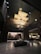 A modern interior space with an artistic ceiling structure made of layered, golden panels. The walls feature vertical stripes and there is a large, square coffee table centered in the open area. Dim lighting and elegant furniture create a luxurious atmosphere.