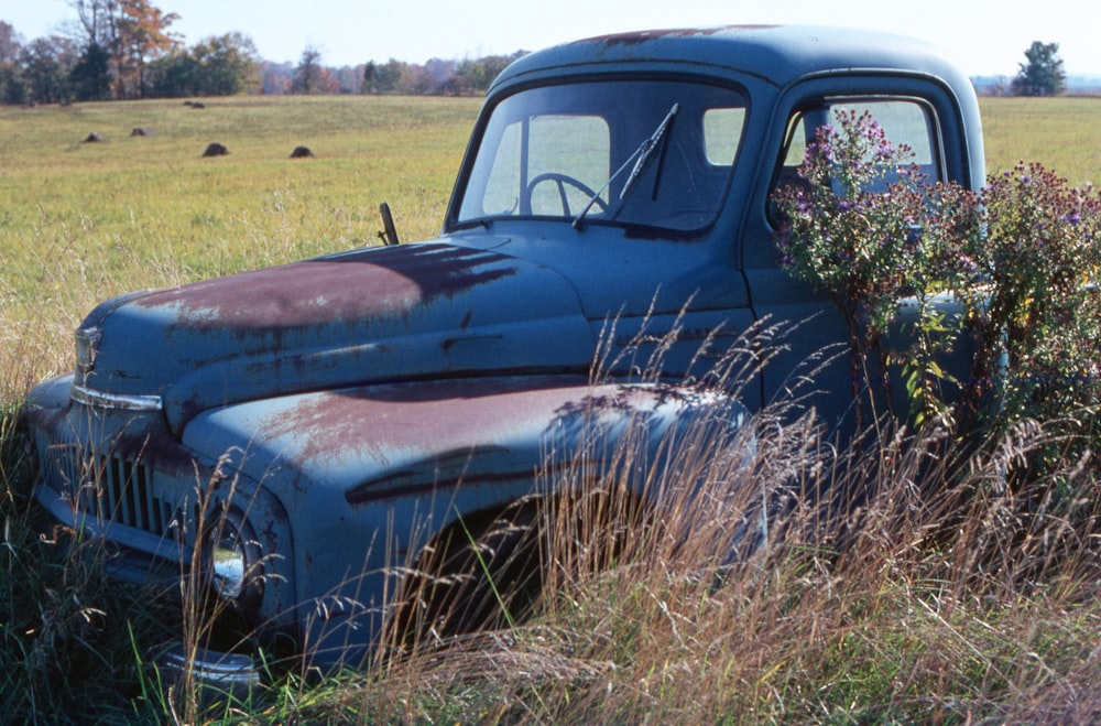an old blue truck is sitting in a field