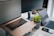 A workspace setup featuring a laptop with its screen slightly open, a tablet, a smartphone, and a wireless keyboard on a desk. A potted green plant adds a touch of nature to the sleek and modern tech environment. Multi-screen setup suggests a focus on productivity.