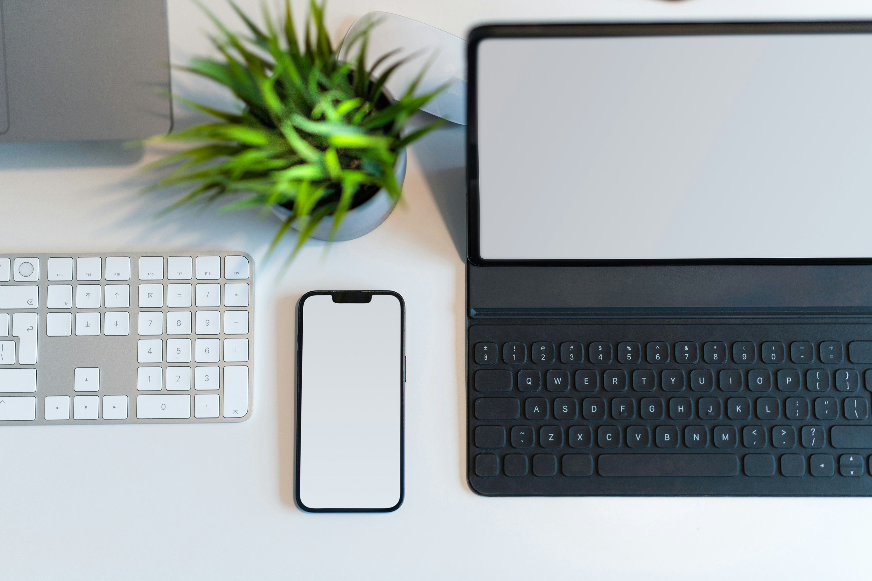 a desk with a keyboard, phone and a plant
