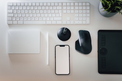 a desk with a keyboard, mouse, cell phone and a plant