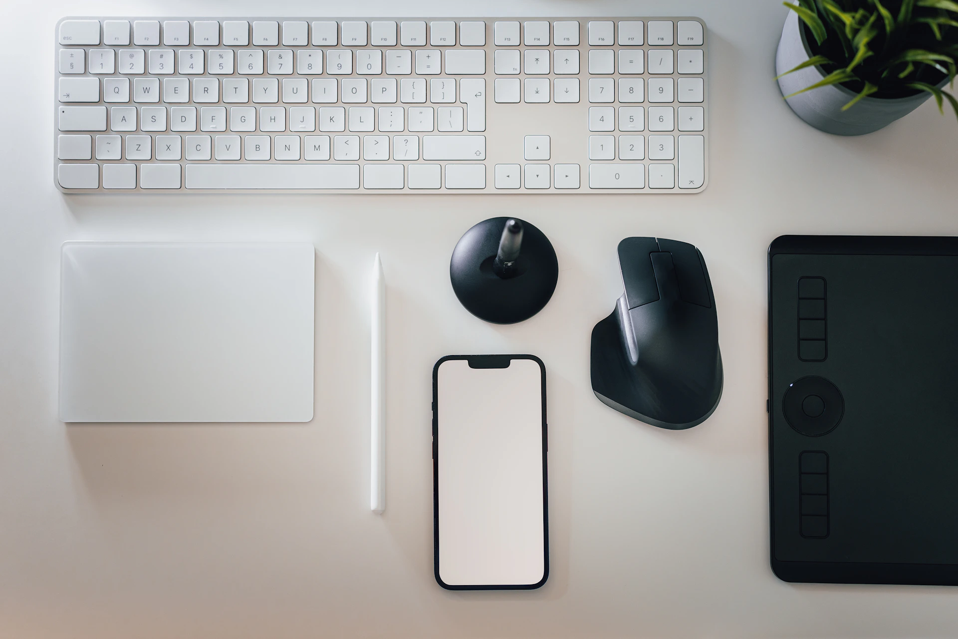 a desk with a keyboard, mouse, cell phone and a plant