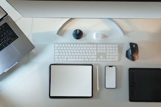 An organized workspace featuring a laptop, desktop monitor, wireless keyboard, a mouse, tablet, smartphone, and stylus pen. The setup looks clean and minimalistic, emphasizing technology and productivity.