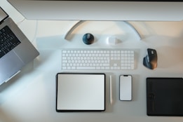 An organized workspace featuring a laptop, desktop monitor, wireless keyboard, a mouse, tablet, smartphone, and stylus pen. The setup looks clean and minimalistic, emphasizing technology and productivity.