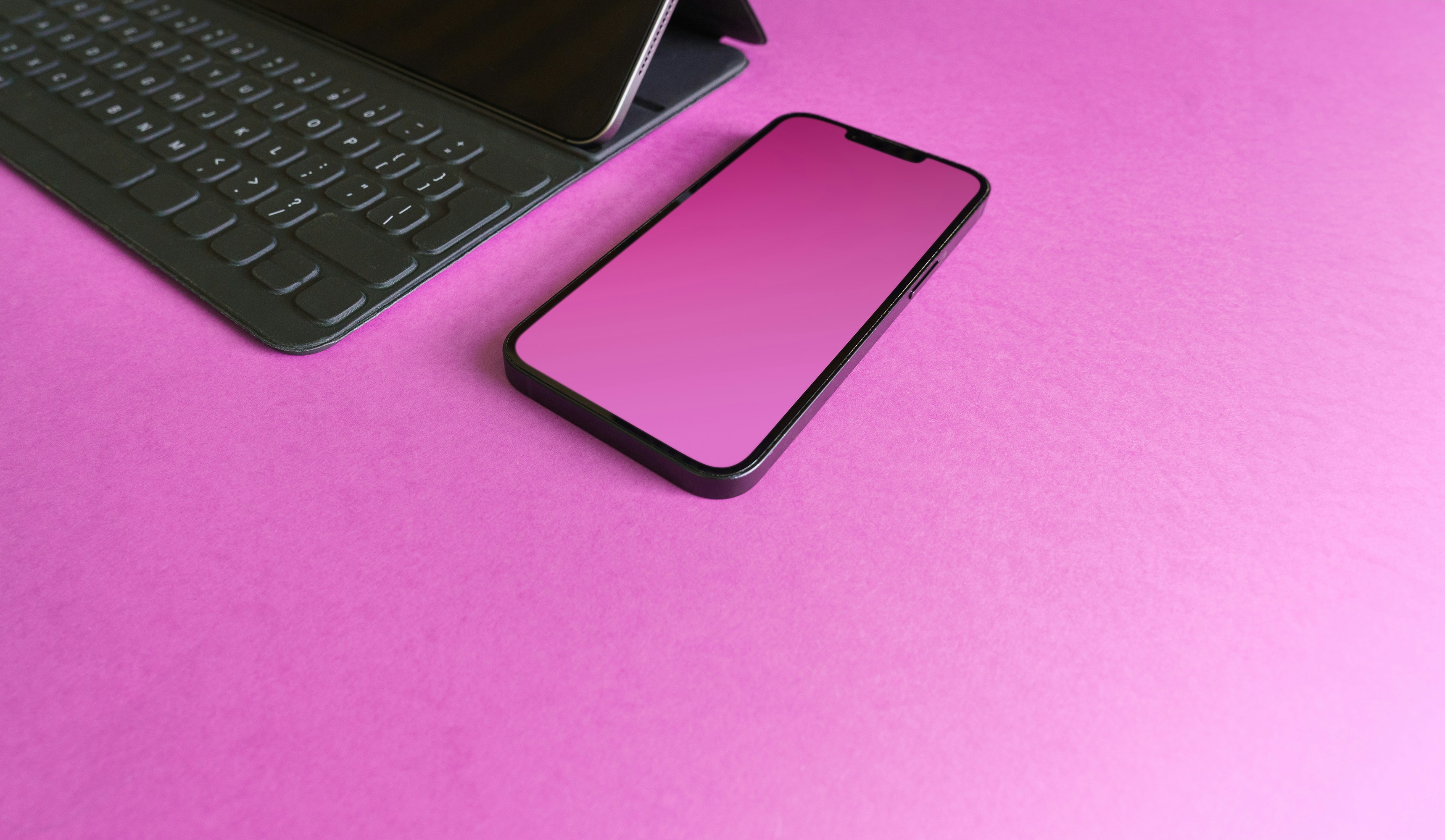 a cell phone sitting next to a keyboard on a pink surface