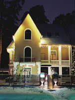 A charming house with lights tracing the front outline, roof ridges, and peaks glowing softly.