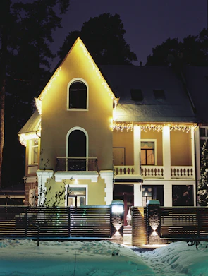 A charming house with lights tracing the front outline, roof ridges, and peaks glowing softly.