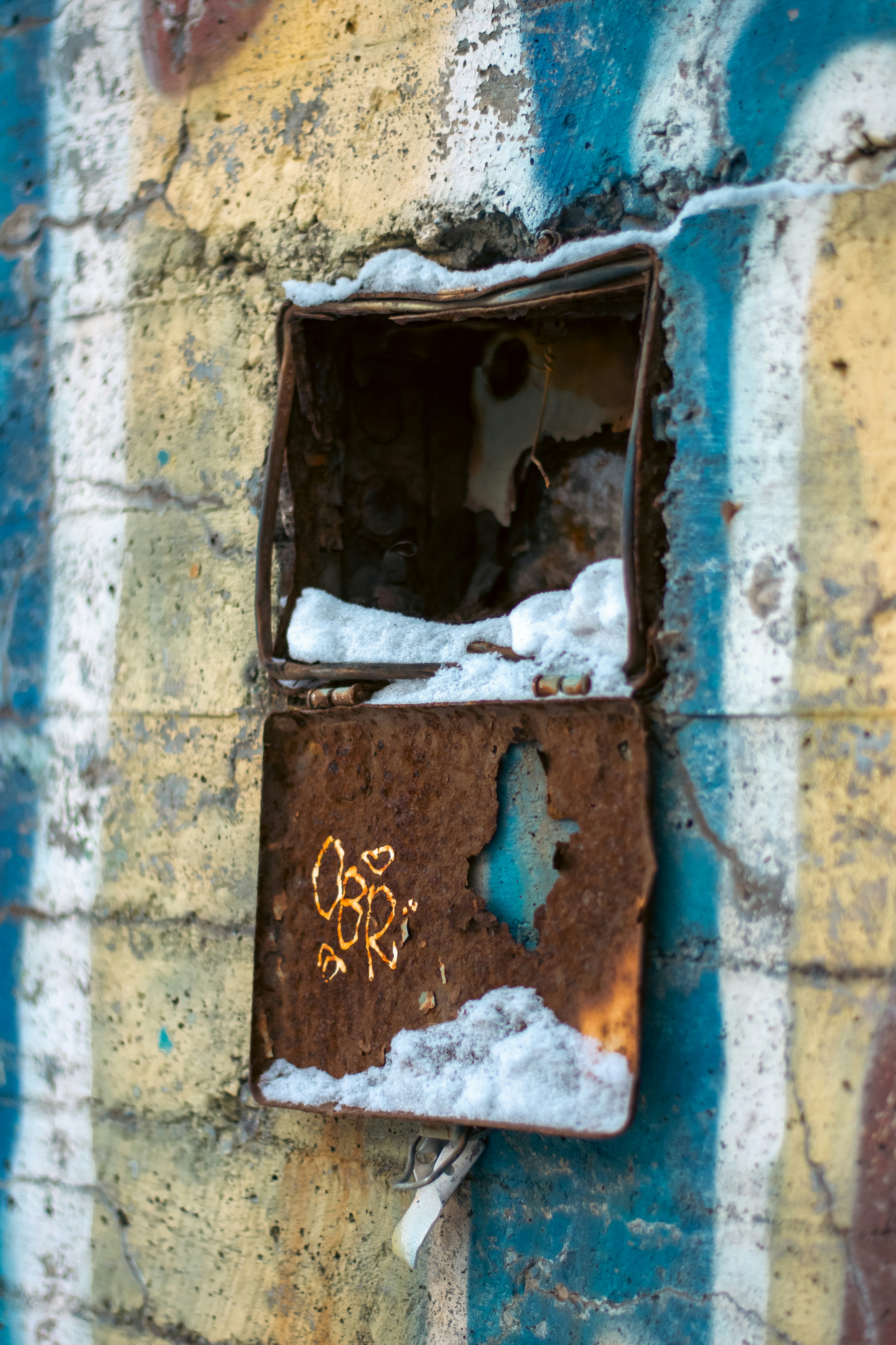 a rusted metal box with graffiti on a brick wall