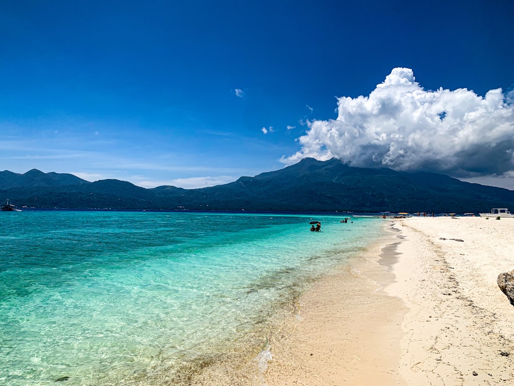 a beach with clear blue water and mountains in the background