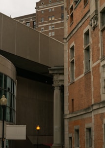 Tall urban buildings with varying architectural styles, including a mix of modern and older designs. A streetlight with a glowing orange bulb stands in the foreground. Brickwork and large windows characterize the structures, contributing to the city's architectural diversity.