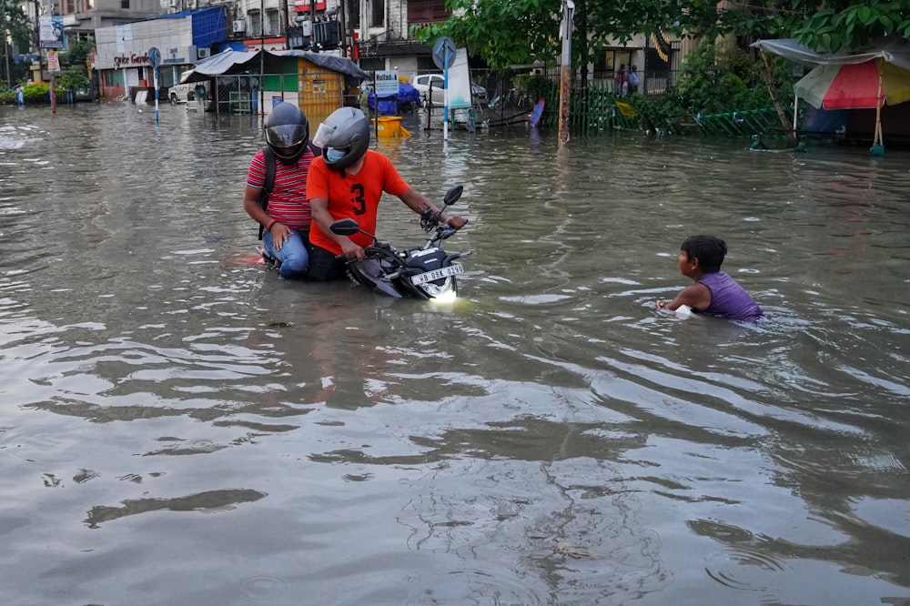 a couple of people riding a motorcycle through a flooded street