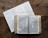 A wooden table holds an open book displaying text, likely a Bible, accompanied by a paper with a reading schedule or chart listing books and chapters.