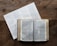 A wooden table holds an open book displaying text, likely a Bible, accompanied by a paper with a reading schedule or chart listing books and chapters.