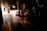 Young ballerinas in tutus are waiting backstage as a performance is underway, with warm lighting highlighting the stage and casting shadows in the wings.