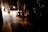 Young ballerinas in tutus are waiting backstage as a performance is underway, with warm lighting highlighting the stage and casting shadows in the wings.