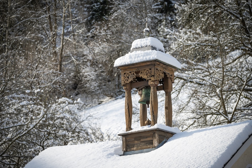 um sino de madeira no topo de um telhado coberto de neve