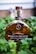 A bottle of Woodford Reserve Kentucky Straight Bourbon Whiskey is centered among green foliage. The bottle is a distinctive shape with a wooden cork, and the label is clearly visible. The background is blurred, drawing focus to the bottle.
