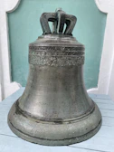Close-up of a polished brass bell with intricate carvings resting on a wooden mandir shelf.