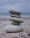 A stack of five smooth, gray stones balanced on top of each other against a blurry seascape backdrop. The stones vary in size, with the largest at the bottom and the smallest at the top. The scene conveys a sense of tranquility and balance.
