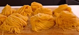 Neatly arranged nests of fresh, yellow pasta sit on a wooden surface, ready for cooking.