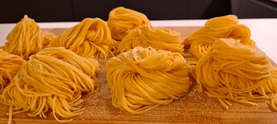 Neatly arranged nests of fresh, yellow pasta sit on a wooden surface, ready for cooking.