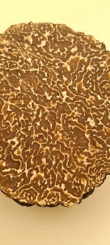 A close-up view of a sliced truffle displaying a marbled, intricate pattern with shades of brown and white against a light yellow background.