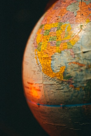 A close-up of a globe highlighting the North American continent, particularly the United States and Mexico. The surface has detailed geographical and political borders, with country names and cities marked. Warm, ambient lighting creates a cozy, vintage atmosphere, casting shadows and reflections on the globe&rsquo;s surface.