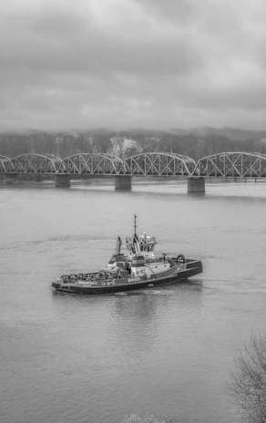 An old towboat cutting through misty river waters under a muted, overcast sky.