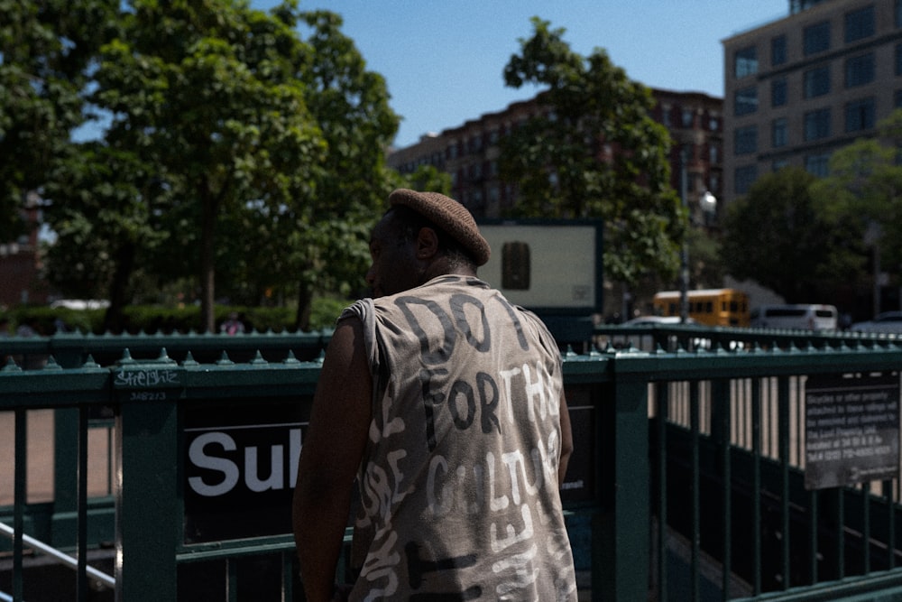 a man walking down a street next to a green fence