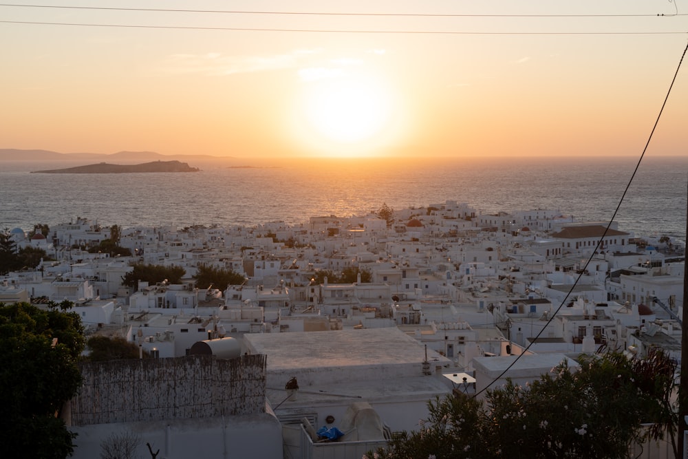 the sun is setting over a city by the ocean