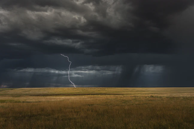 Thunderstorm clouds gathering over a vast open field with lightning striking