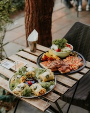 A rustic wooden table with plates of sandwiches, salads, and fresh coffee in the garden.