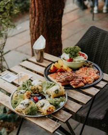 A rustic wooden table with plates of sandwiches, salads, and fresh coffee in the garden.