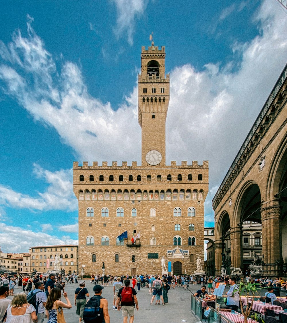 a crowd of people walking around a building with a clock tower