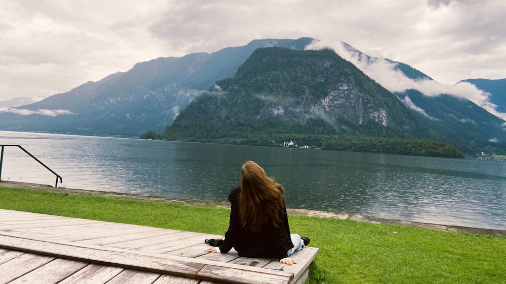 a woman sitting on a bench looking out over a lake
