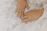 Close-up of perfectly manicured hands with soft pink nails resting on a white linen cloth.