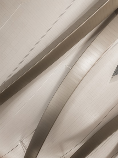 An abstract architectural structure featuring curved metallic beams and sleek, smooth surfaces. The design appears modern and minimalist, with light reflecting off the metallic surfaces.