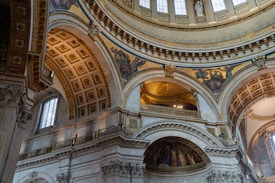 Elaborate architectural details featuring grand arches and intricate moldings, embellished with stunning frescoes and statues. The interplay of light and shadows highlights the elegance of the ornate ceiling patterns.