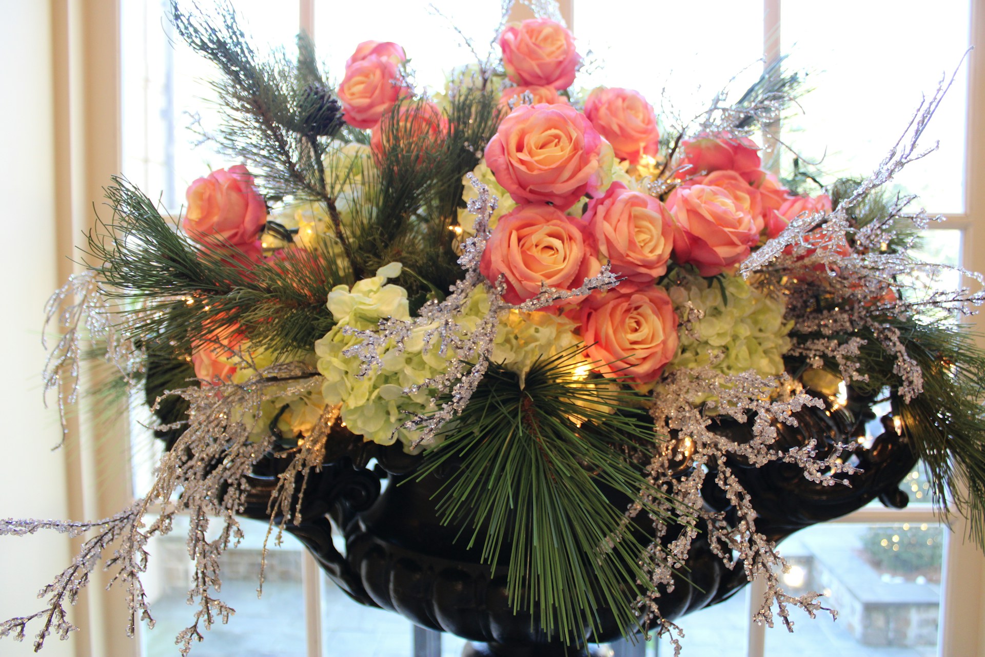 An elegant wedding centerpiece with soft peach roses, dark brown branches, and sage green foliage, glowing warmly in natural light.