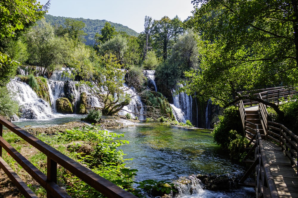 a wooden bridge over a river next to a waterfall