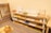 A neatly organized classroom shelf contains a variety of educational materials and tools. There are wooden trays, colored boxes, abacuses, and charts. Each shelf is filled with learning aids, prominently featuring items like math boards and counting tools. The environment is bright and has a warm, inviting atmosphere typical for a Montessori setting.