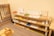 A neatly organized classroom shelf contains a variety of educational materials and tools. There are wooden trays, colored boxes, abacuses, and charts. Each shelf is filled with learning aids, prominently featuring items like math boards and counting tools. The environment is bright and has a warm, inviting atmosphere typical for a Montessori setting.