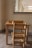 A small wooden table and chair set placed against a wall, with a window partially visible behind it. On top of the table, there is a wooden educational toy with small pegs, possibly for sorting or counting.